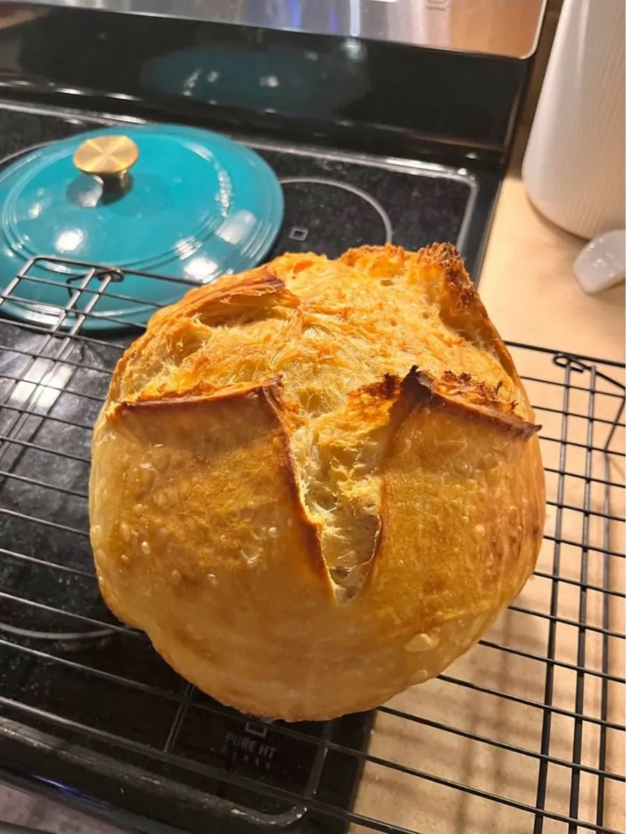 Golden sourdough loaf on a rack next to a dutch oven